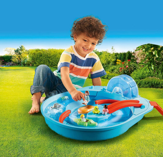 Young child playing with Playmobil Aqua 1.2.3 water playset outdoors on grass, interacting with floating toy figures and boats